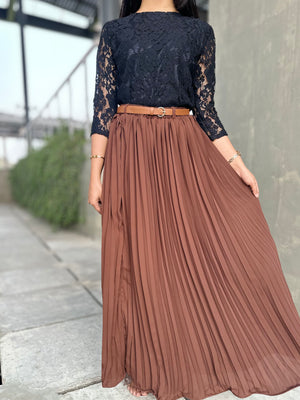 Person wearing a black lace top and brown pleated skirt outdoors.