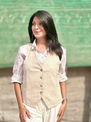 Woman wearing a beige vest over a white shirt with a blurred green background