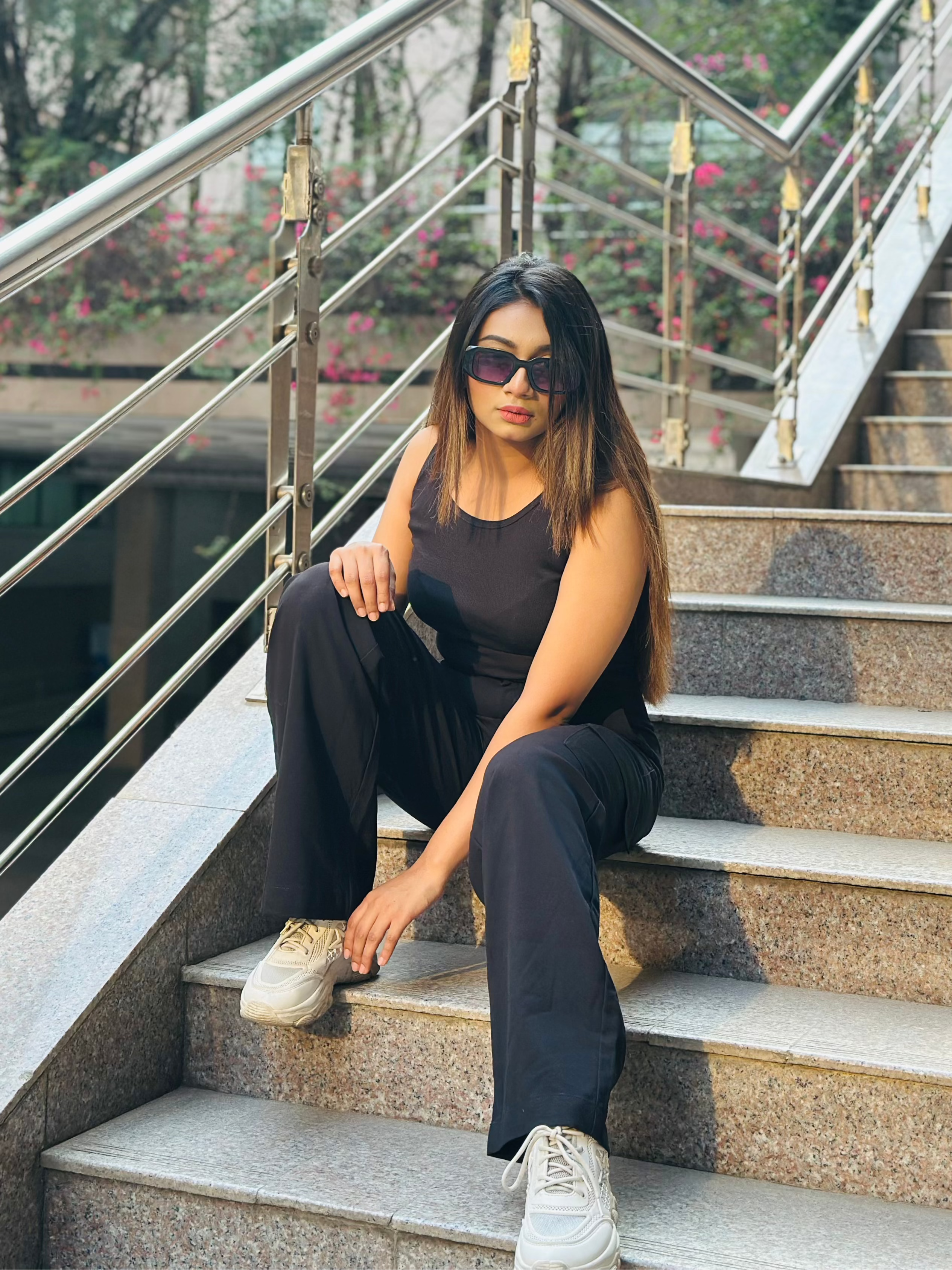 A person wearing a sleeveless tan crop top and black pants, seated on outdoor stairs.