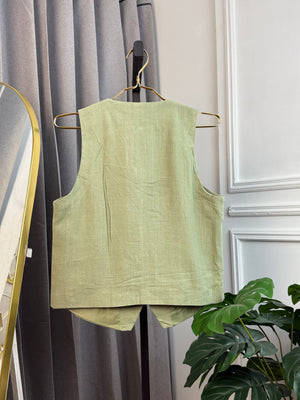 Light green sleeveless top on a hanger against a neutral background with a plant.