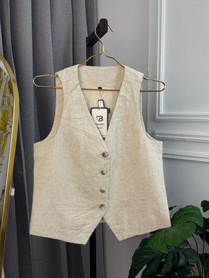 Beige vest on a hanger against a gray curtain background