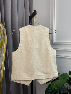 Beige sleeveless top on a hanger against a gray curtain background