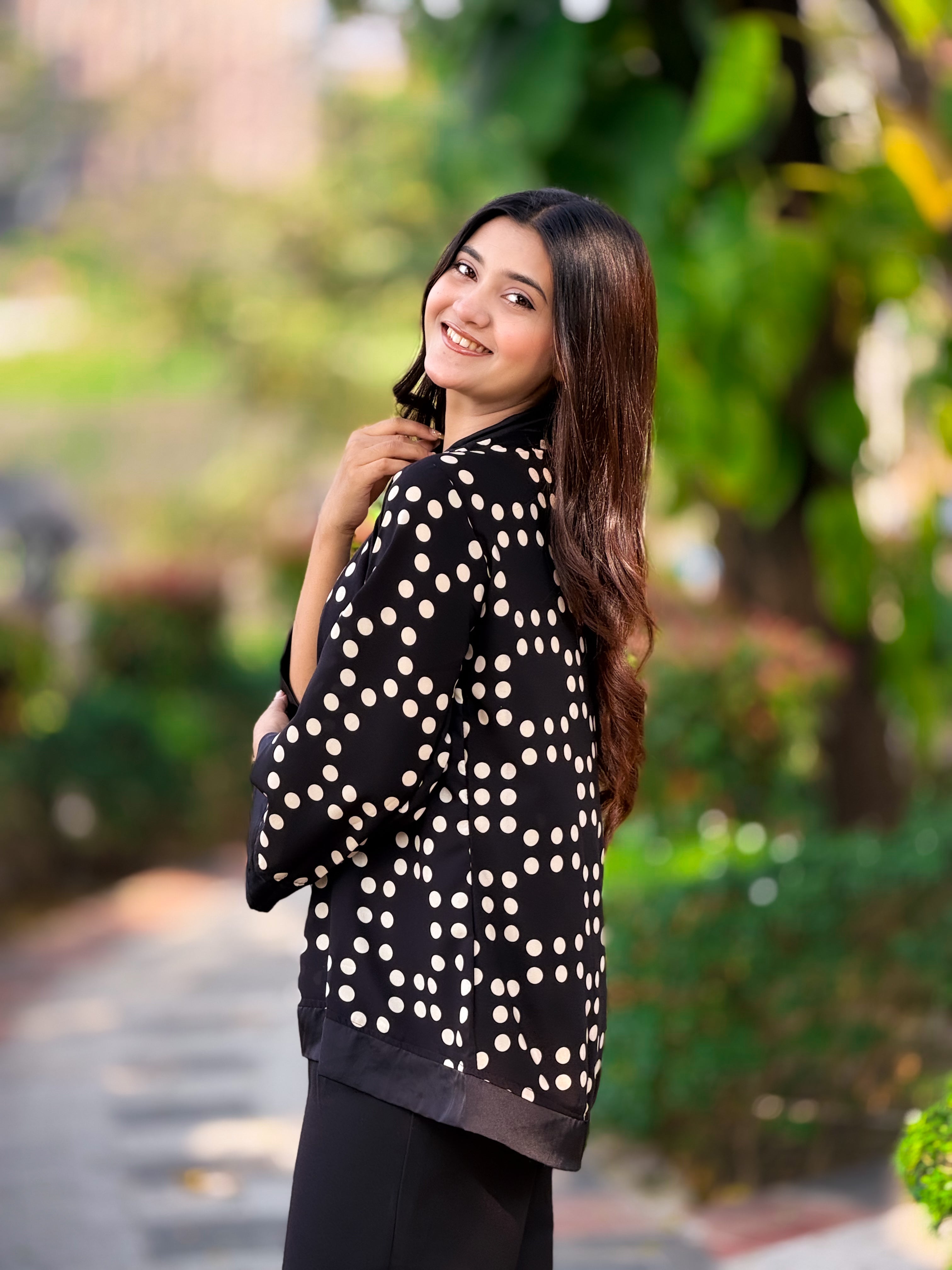 Woman wearing a black and white polka dot top outdoors with greenery in the background
