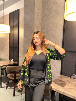 Woman posing in a modern interior setting with tables and chairs wearing our Black Green Polka Dot Kimono.