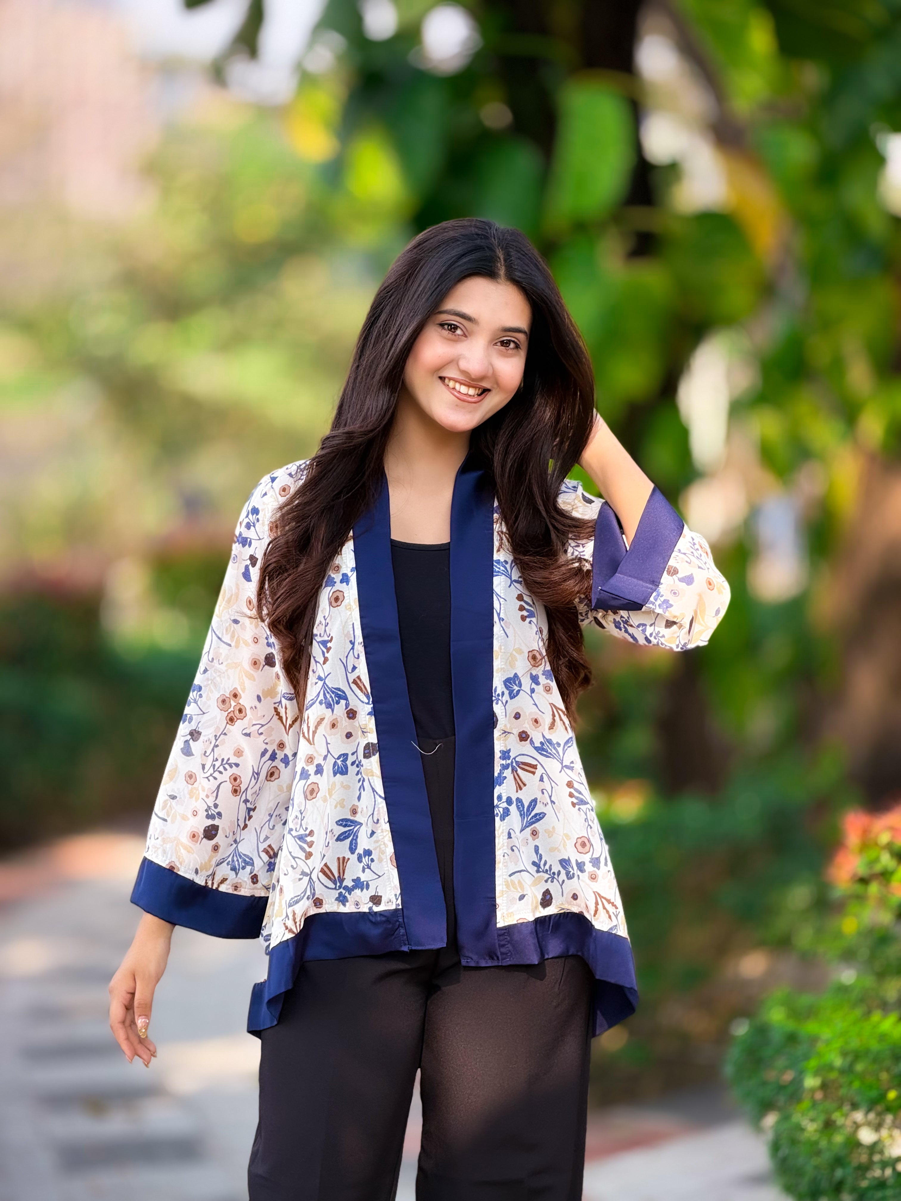 Woman wearing a floral kimono-style jacket outdoors with greenery in the background