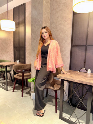 Woman posing in a modern cafe setting with tables and chairs by wearing our Misty polka dot Kimono over a black top.
