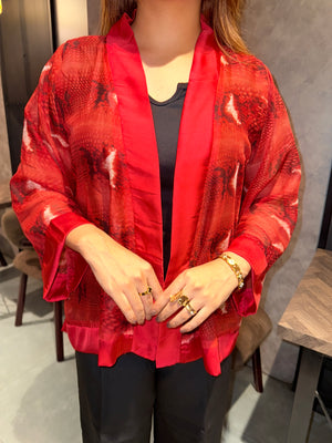 Person wearing ared snake print kimono with gold jewelry on a wooden floor.