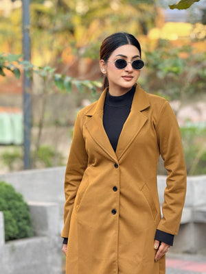 Woman wearing a mustard yellow coat and sunglasses outdoors.