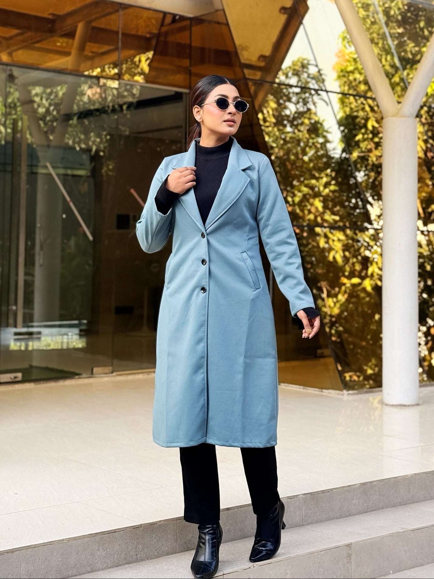 Woman in a light blue coat walking outdoors near modern architecture
