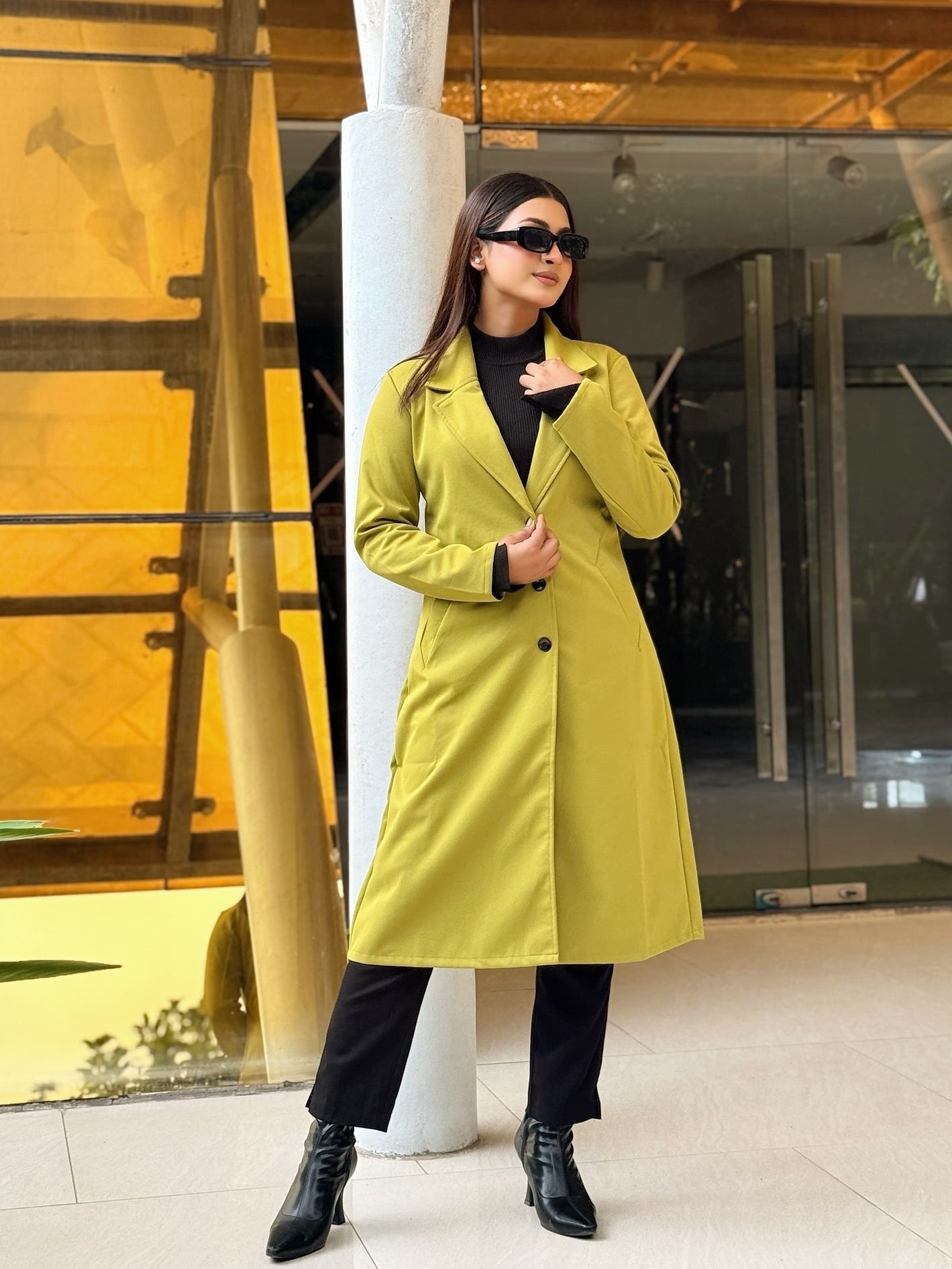 Person wearing a bright yellow coat standing in front of a modern building with yellow interior.