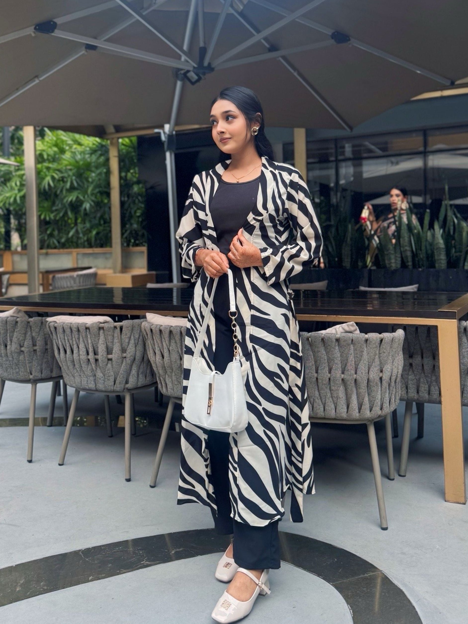 Woman in a zebra-patterned long shrug standing outdoors under an umbrella