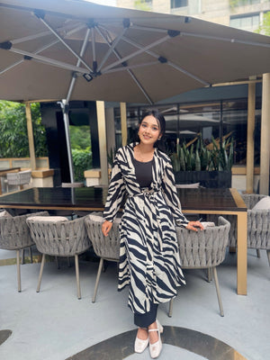 Woman in a zebra print long shrug sitting at an outdoor dining table with a large umbrella.