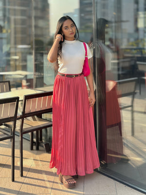 Woman in a white top and pink pleated skirt standing on a rooftop with cityscape background