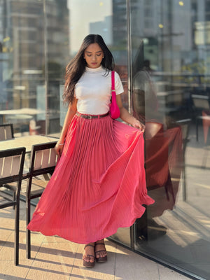 Woman in a white top and pink pleated skirt standing on a balcony with cityscape background