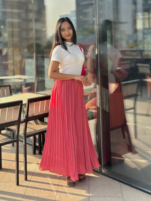 Woman in a white top and pink pleated skirt standing in front of a glass door with reflections.