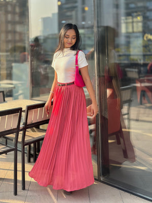 Woman in a white top and pink pleated skirt standing in front of a glass door.