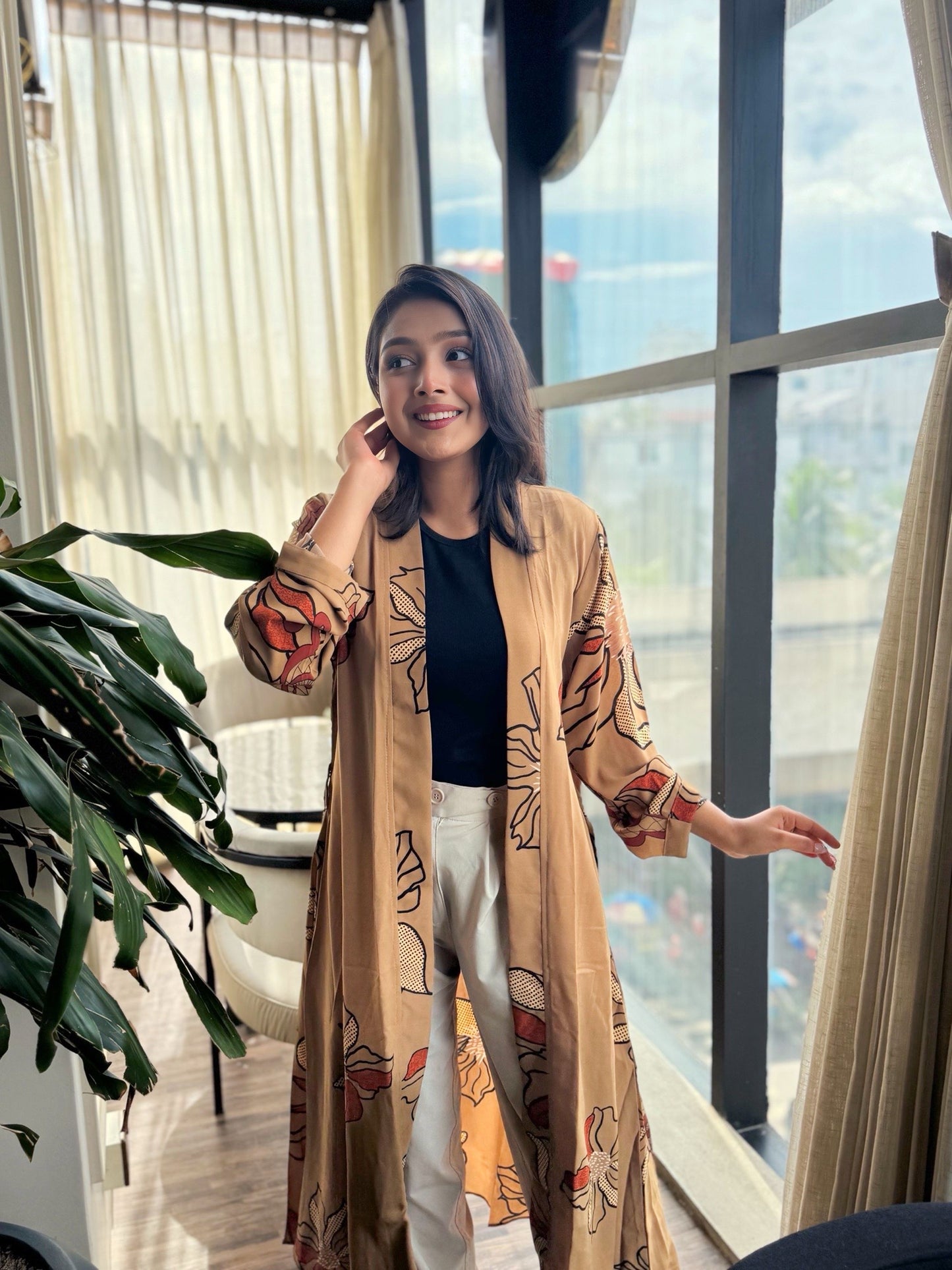 Woman in a stylish outfit standing by a large window with a cityscape view.