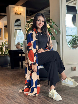Woman sitting in a modern interior setting wearing a colorful patterned long shrug.