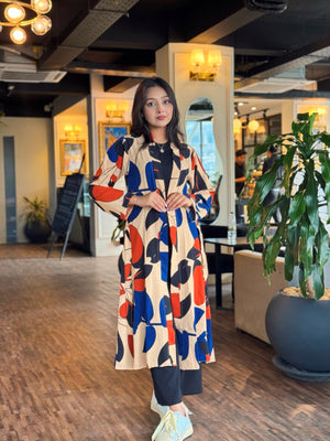 Woman in a colorful long shrug standing in an indoor setting with plants and furniture.