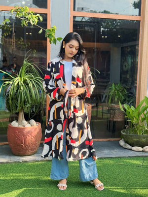 Woman wearing a patterned long shrug standing outdoors with plants and a building in the background