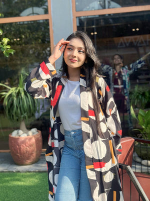 Woman wearing a patterned long shrug outdoors with plants and a building in the background