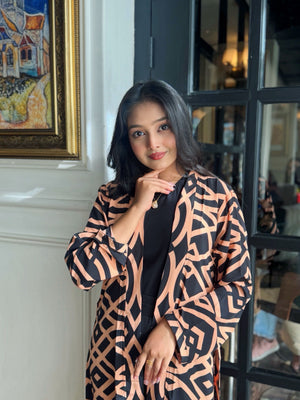 Woman wearing a Woman wearing a long shrug outerwear in black and orange standing in front of a glass door.