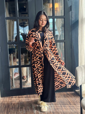 Woman wearing a Woman wearing a long shrug outerwear in black and orange standing in front of a glass door.