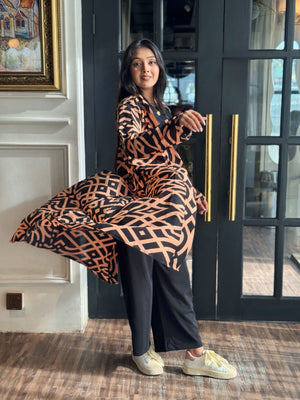 Woman wearing a Woman wearing a long shrug outerwear in black and orange standing in front of a glass door.