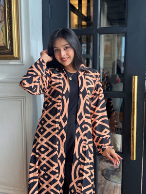 Woman wearing a Woman wearing a long shrug outerwear in black and orange standing in front of a glass door.