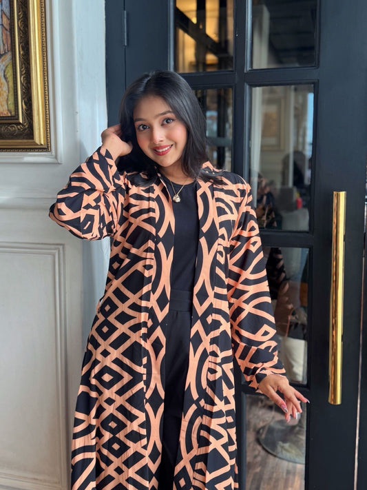 Woman wearing a Woman wearing a long shrug outerwear in black and orange standing in front of a glass door.