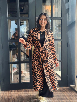 Woman wearing a Woman wearing a long shrug outerwear in black and orange standing in front of a glass door.