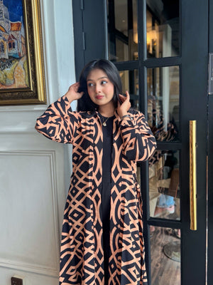Woman wearing a long shrug outerwear in black and orange standing in front of a door.