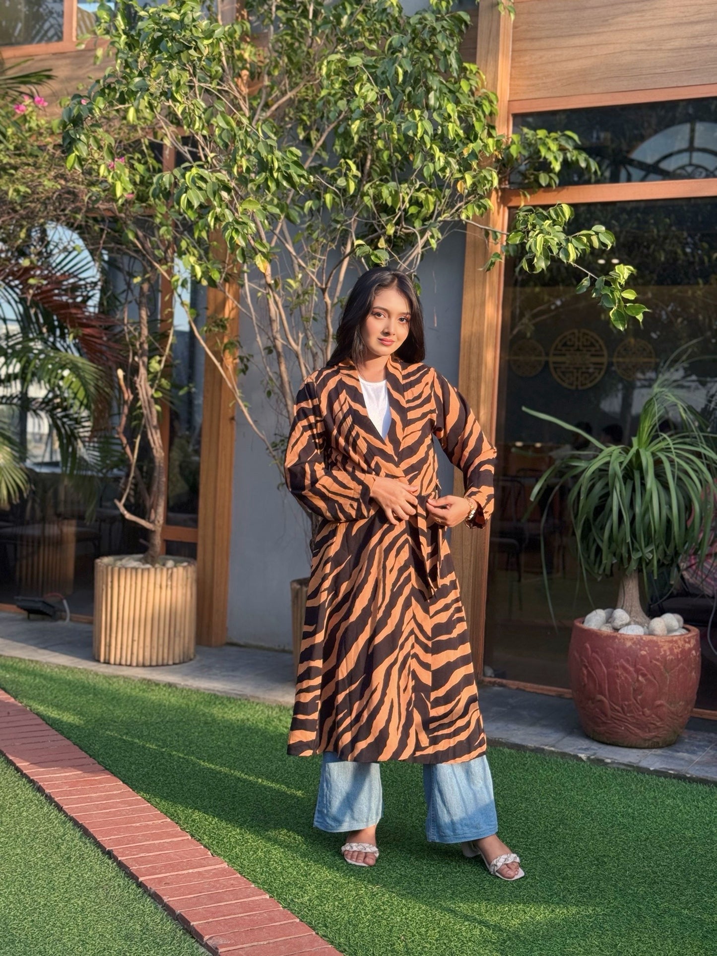 Woman wearing a tiger-striped long shrug standing outdoors with plants and a building in the background