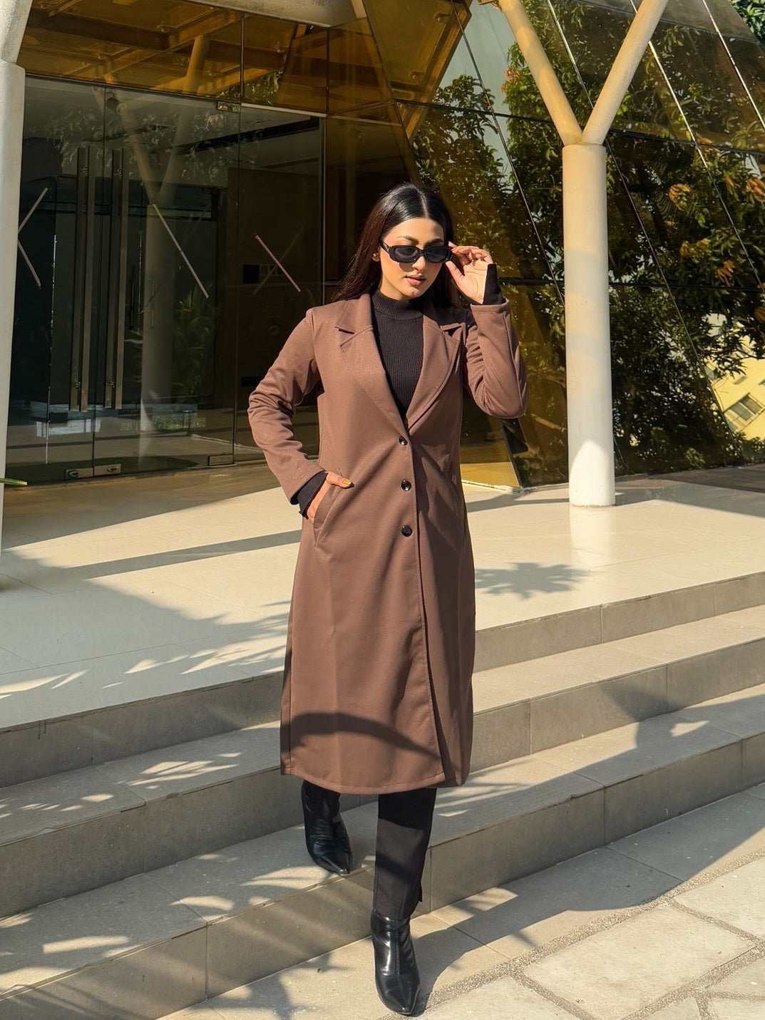 Person standing in front of a modern building with a glass facade and wooden beams.
