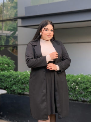 Woman in a black coat standing outdoors with a building and greenery in the background