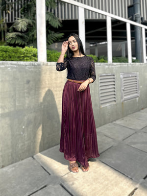 Woman in a black top and purple pleated skirt standing outdoors on a sidewalk.