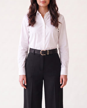 A woman wearing a white long-sleeve button-down shirt tucked into black wide-leg trousers, styled with a black textured belt featuring a gold buckle, against a plain off-white background.