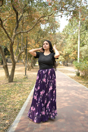 Woman in a black dress with a purple floral skirt standing on a path with trees in the background TrendyBuzz