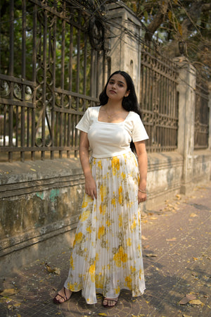Woman in a white dress with yellow floral pattern standing on a textured surface.