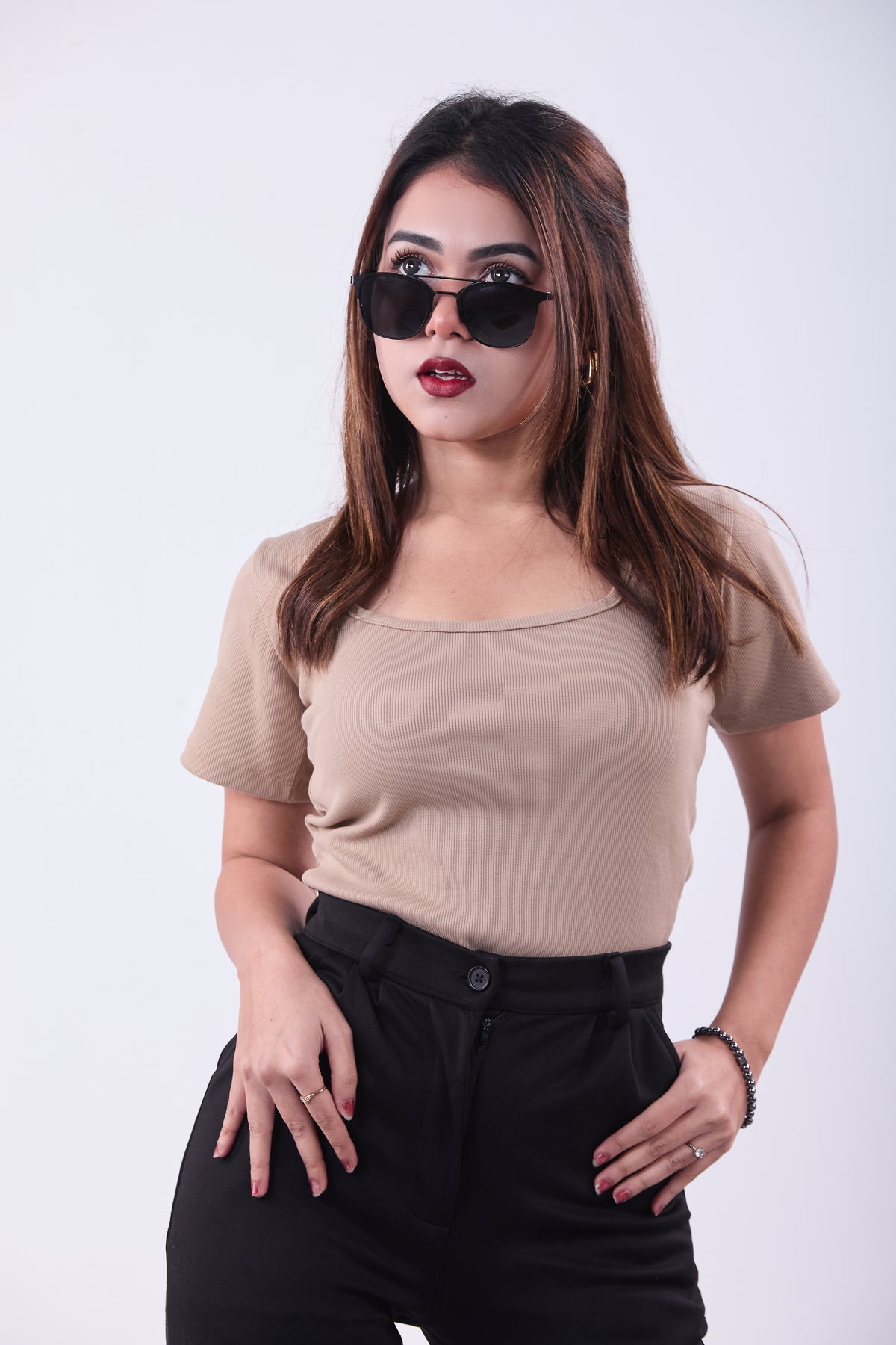 Woman wearing a beige top and black pants with sunglasses on a white background