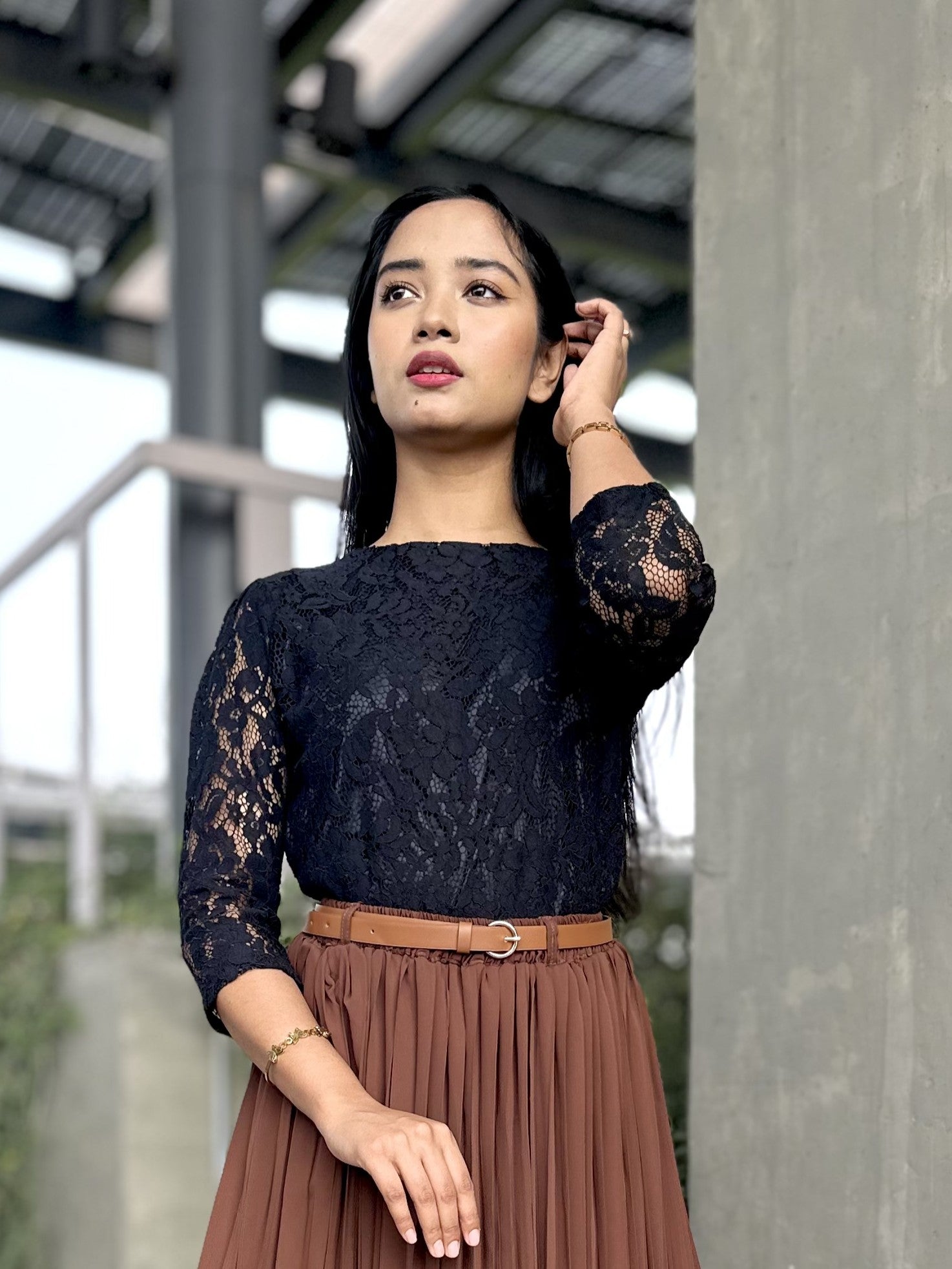Woman wearing a black lace top and brown skirt outdoors.