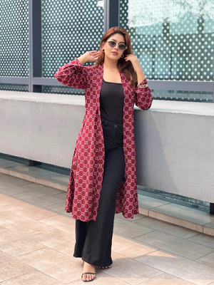 Woman wearing a red patterned Shrug and black pants standing against a modern building.