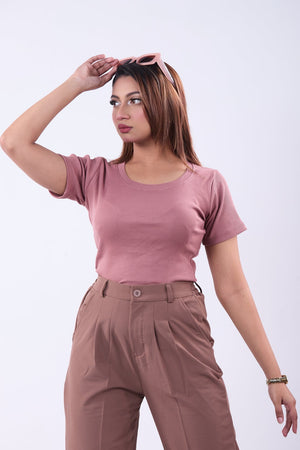 Woman wearing a pink top and brown pants against a white background