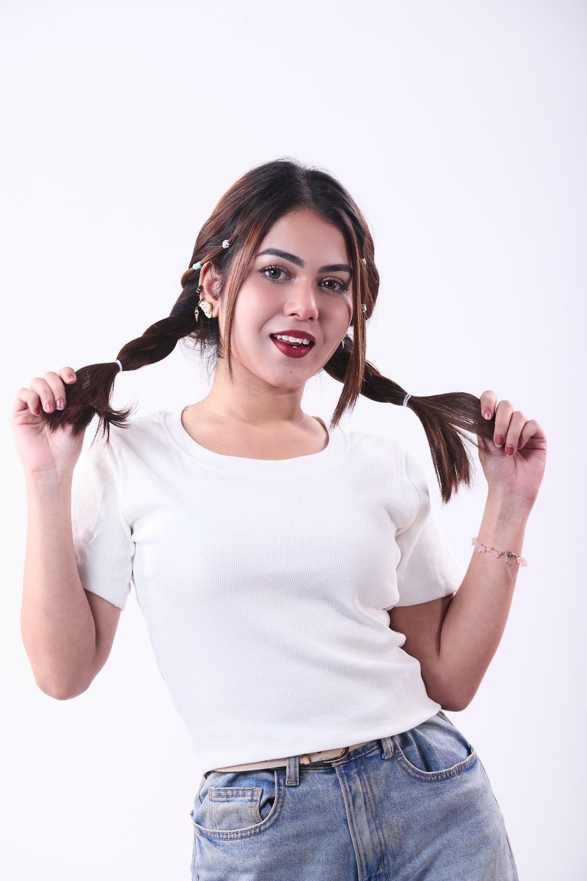 Woman with pigtails wearing a white shirt and blue jeans on a white background