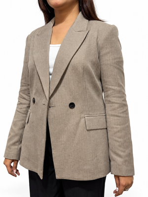 A woman wearing a light taupe double-breasted blazer over a white top and black pants, shown from the neck down against a plain white background.