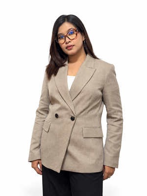 A woman wearing a light beige double-breasted blazer over a white top and black trousers, standing against a plain white studio background.