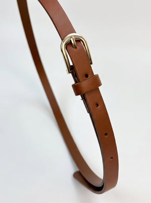 A close-up of a brown leather strap, likely a belt or strap accessory, featuring a polished gold-tone metal buckle and a matching leather keeper loop, set against a plain white background.