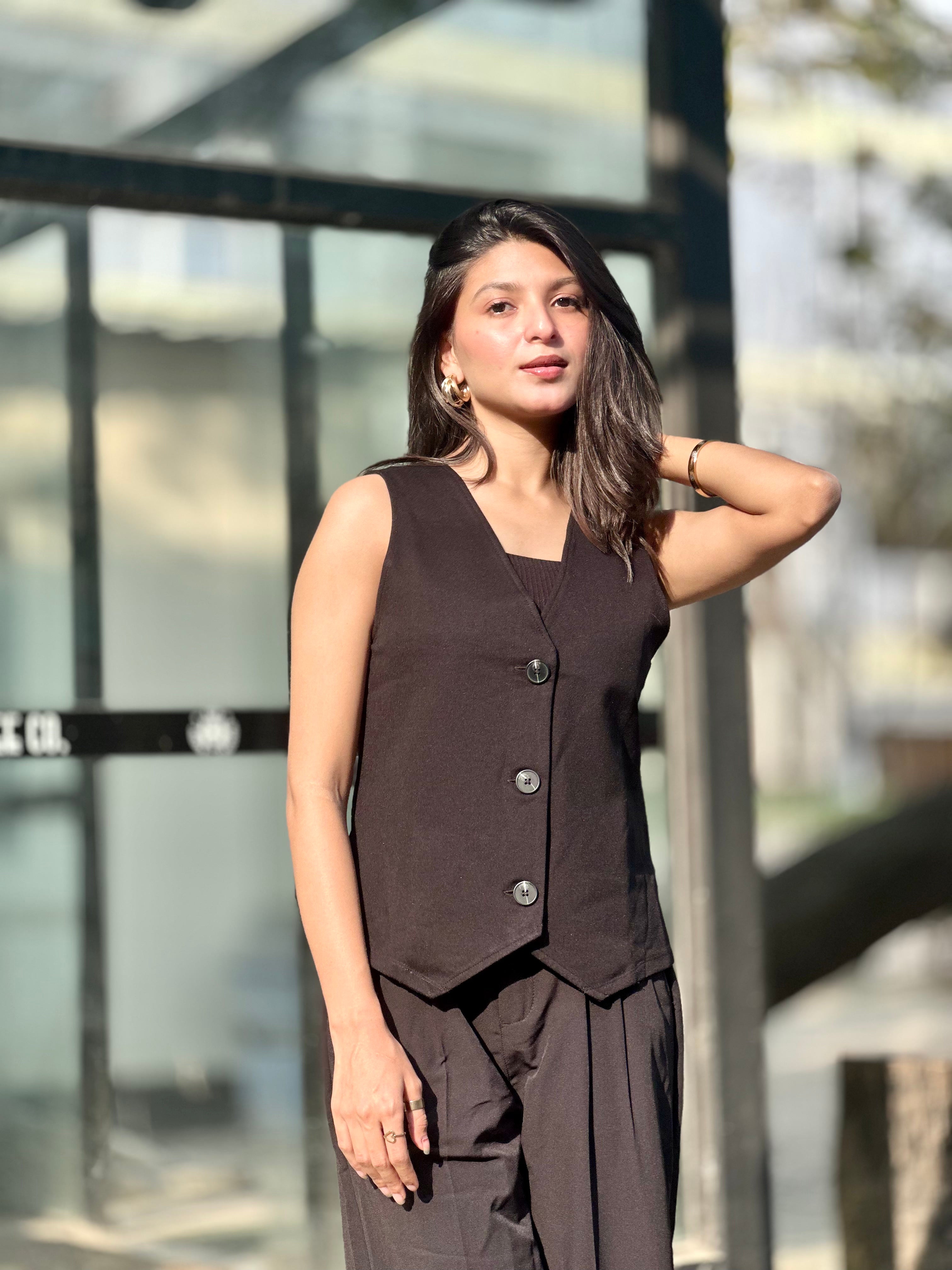Woman wearing a brown sleeveless top and pants standing outdoors.