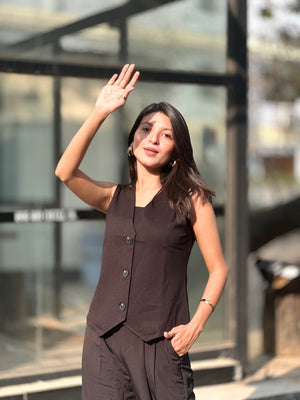 Woman in a black sleeveless top and pants waving outdoors.