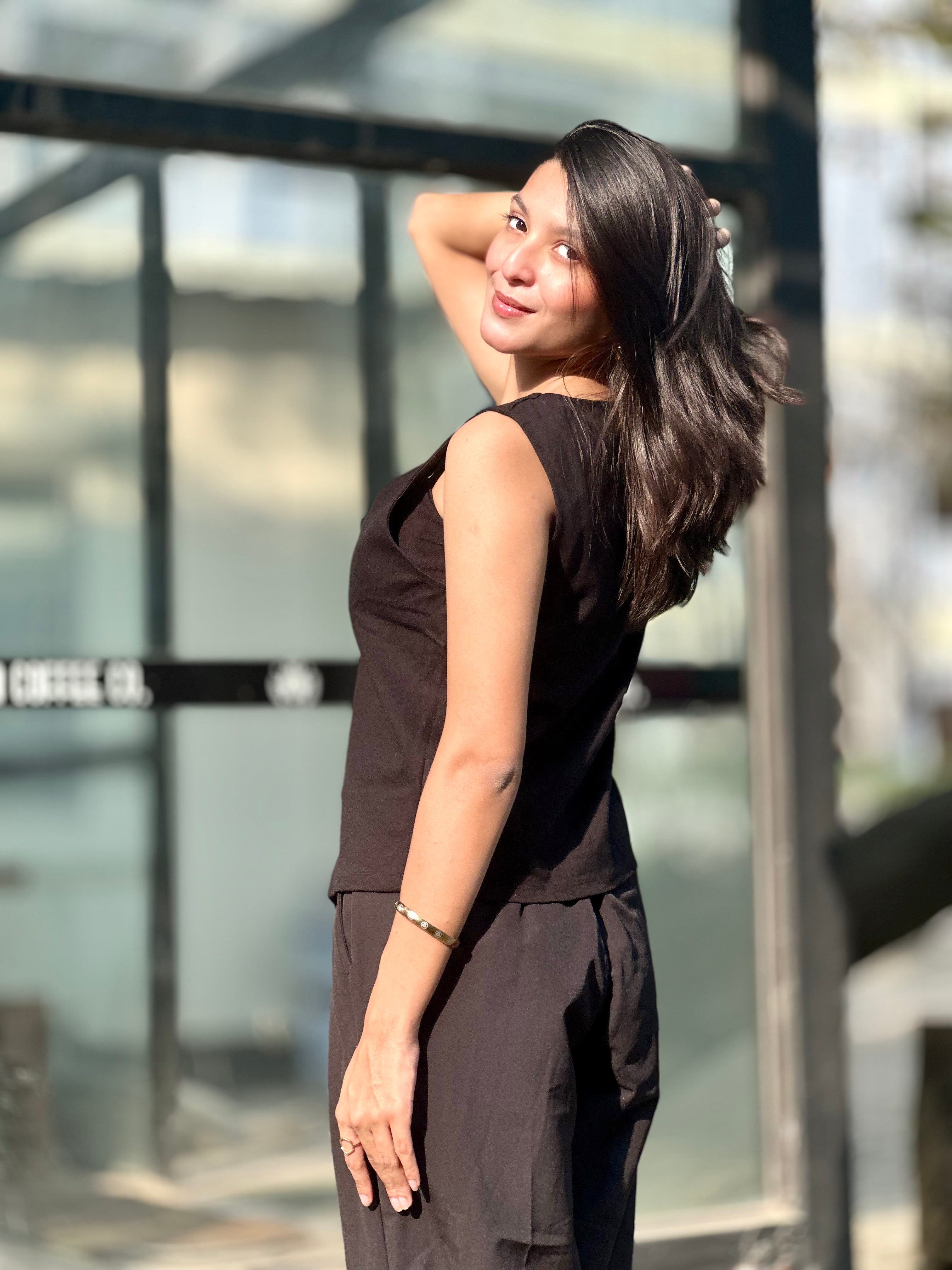 Woman in a black sleeveless top and pants standing outdoors with a blurred background
